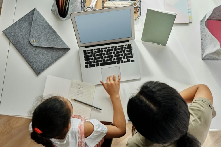 A mother helps her daughter with schoolwork on a laptop at home, promoting education and bonding.